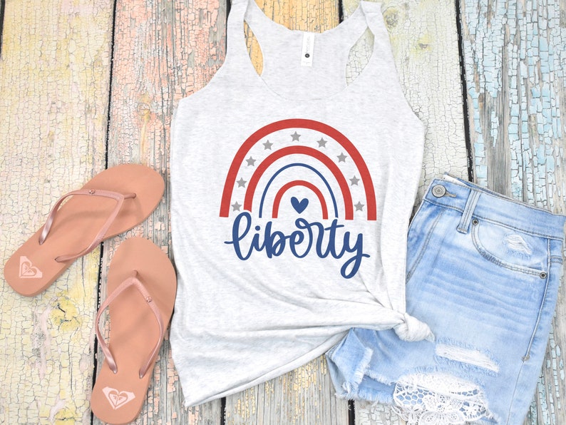 K&ouml;nnte beinhalten: Ein graues Tanktop mit einem rot-wei&szlig;-blauen Regenbogenmuster und dem Wort "liberty" in blauer Schrift. Der Regenbogen hat wei&szlig;e Sterne und ein kleines blaues Herz in der Mitte.