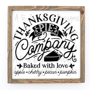 May include: A brown wooden framed sign with a white background and black text that reads "Thanksgiving Pie Company Baked with love apple. cherry. pecan. pumpkin". The sign features a stylised pie with a crust and a decorative banner that reads "Pie".