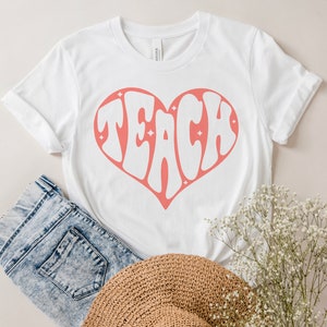 May include: White t-shirt with a pink heart design that says "TEACH" inside the heart.