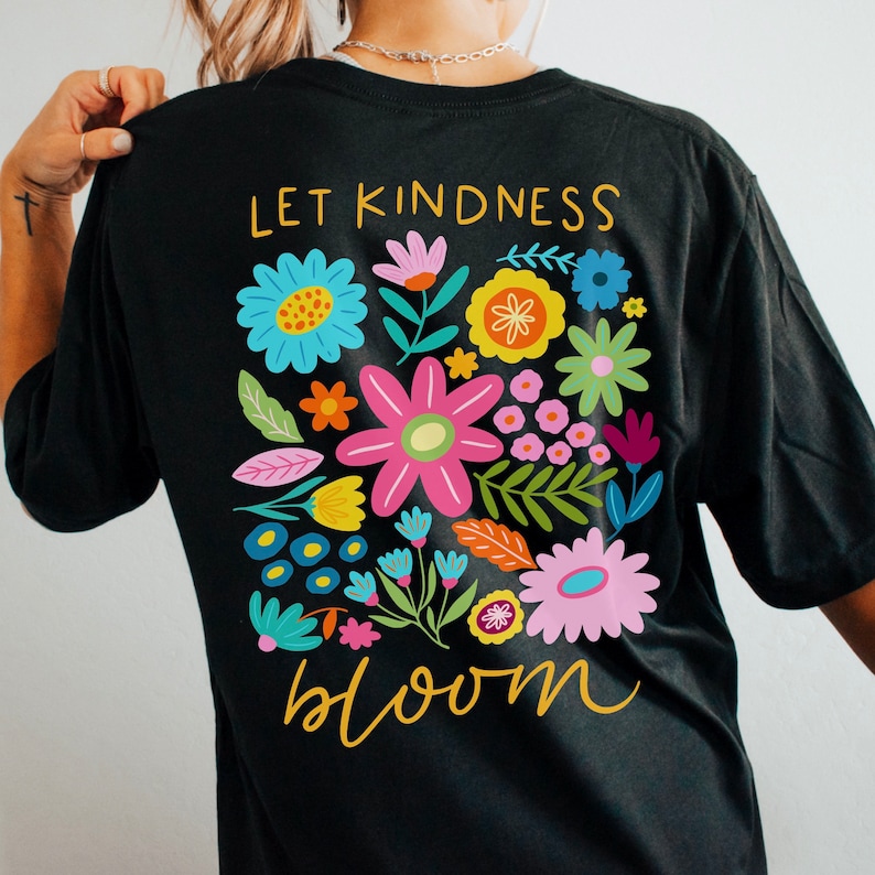 Peut inclure: T-shirt noir avec un motif floral color&eacute; et le texte "Let kindness bloom" en lettres dor&eacute;es.