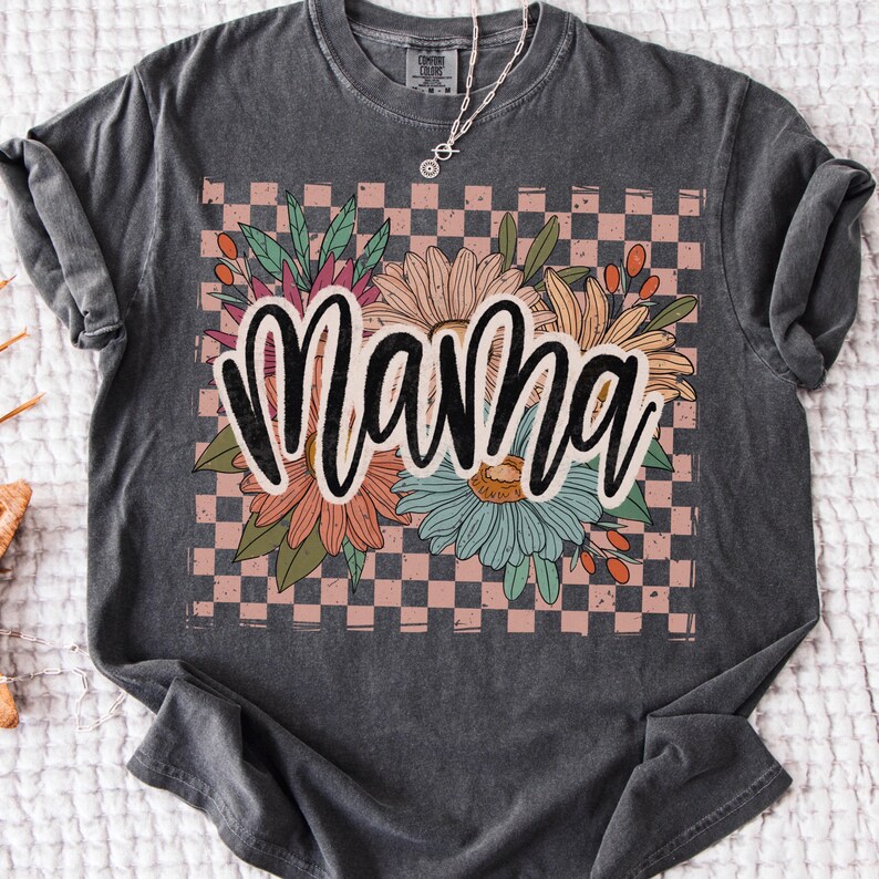Pode incluir: Uma camiseta cinza escura com um design floral e a palavra "mama" em letras pretas. O design floral est&aacute; sobre um fundo xadrez rosa e branco.
