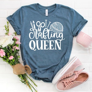 May include: A blue t-shirt with white text that says "Wool Crafting Queen" with a yarn ball and knitting needles graphic.
