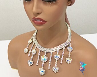 Pode incluir: Um colar choker de strass prateado com um design em cascata. O colar apresenta várias filas de strass e uma franja de strass maiores.