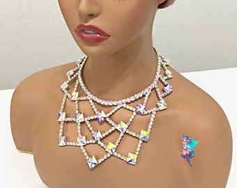 May include: A silver crystal choker necklace with a geometric design. The necklace is made of small, square-shaped crystals that are connected by thin metal chains. The necklace is worn by a mannequin with a pink and black wig.