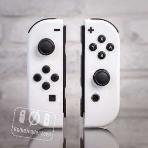 May include: A pair of white Nintendo Switch Joy-Con controllers with black buttons. The controllers are separated and facing forward. The left controller has a black analog stick and the right controller has a black button.
