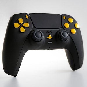 Puede incluir: Un mando de PlayStation 5 negro con botones amarillos. El mando tiene un esquema de color negro y amarillo.
