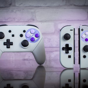 May include: A white Nintendo Switch controller with purple and white buttons, and a pair of white Joy-Con controllers with purple and white buttons.