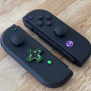 May include: Two black Nintendo Switch Joy-Con controllers with a green and black d-pad on one controller and a purple button on the other.