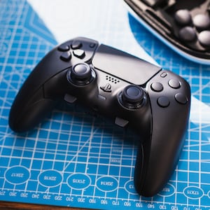 May include: A black wireless game controller with a PlayStation logo. The controller has two analog sticks, a D-pad, and buttons.