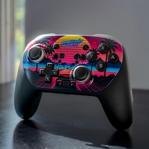 May include: Black gaming controller with a colorful retro design. The controller features a sunset scene with palm trees, a car, and the text "gametrader zero". The buttons are black and the joysticks are gray.