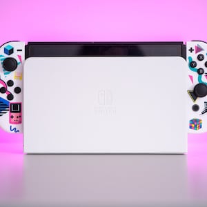 May include: A white Nintendo Switch console with a retro-themed design. The console has a black screen and two white Joy-Con controllers with colorful 80s-inspired graphics. The text "Nintendo Switch" is printed on the console.