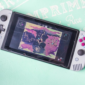 Może przedstawiać: Szara konsola Nintendo Switch z czarnym ekranem wyświetlającym mapę. Konsola ma spersonalizowaną płytkę czołową w kolorze szarym i czarnym oraz zestaw r&oacute;żowych i niebieskich przycisk&oacute;w.