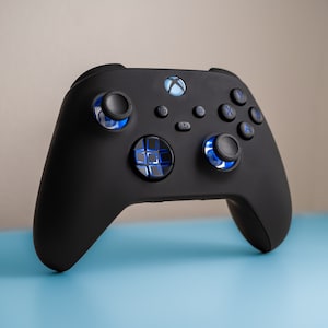 Op de afbeelding: Een zwarte Xbox-controller met blauwe verlichte knoppen. De controller heeft een textuur grip en een standaard lay-out met een D-pad, ABXY-knoppen en triggers.