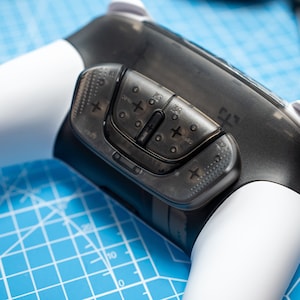 May include: Close-up of a black and white gaming controller with a transparent, textured panel featuring multiple buttons and the text "L2", "R2", "OPT", "PRO", and "5.1".