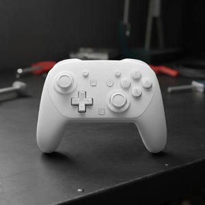 May include: A white wireless game controller with a D-pad, face buttons, and analog sticks. The controller is on a black surface with tools in the background. The controller has a minimalist design.