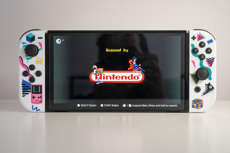 May include: A white Nintendo Switch console with a retro-themed design. The console is displaying a screen with the text "licensed by Nintendo".