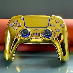 May include: A gold-plated PlayStation 5 DualSense wireless controller with blue accents. The controller has a textured surface and a PlayStation logo on the front.