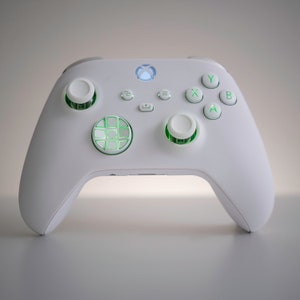 Pode incluir: Um controlador Xbox branco com botões verdes e um padrão de grade verde na placa frontal.
