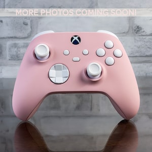 Könnte beinhalten: Ein rosa Xbox-Controller mit weißen Knöpfen und einem weißen Steuerkreuz. Der Controller hat ein rosa-weißes Farbschema.