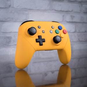 May include: A yellow Nintendo Switch controller with black buttons and a black directional pad. The controller has a textured surface and is designed for gaming.