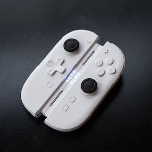 May include: A white gaming controller with black buttons and a directional pad. The controller has a series of small lights and various buttons, including A, B, X, and Y. The controller is designed to be held in two hands.
