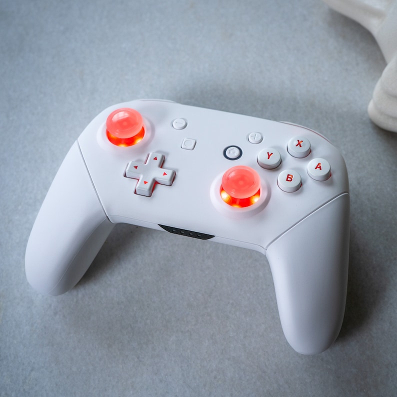 May include: A white Nintendo Switch controller with red buttons. The controller has a D-pad, four face buttons labeled X, Y, B, and A, and two analog sticks.