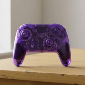 May include: A transparent purple video game controller with visible internal components. The controller features a directional pad, buttons, and analog sticks. The device is resting on a light-colored wooden surface.