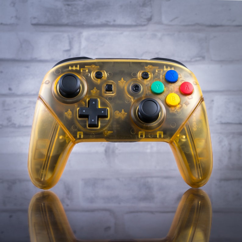 May include: A yellow transparent Nintendo Switch controller with black buttons and a green, blue, red, and yellow button layout.