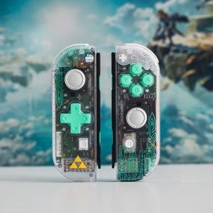 May include: A pair of clear Nintendo Switch Joy-Con controllers with green buttons and a green and white design. The left Joy-Con has a Triforce symbol on the back. The right Joy-Con has a circular pattern on the back.