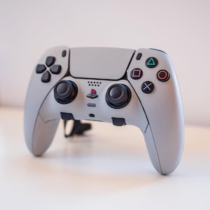 May include: A white PlayStation 5 DualSense wireless controller with black buttons and analog sticks. The controller has a textured grip and a PlayStation logo on the front.