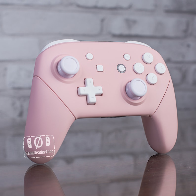 Pu&ograve; includere: Un controller Nintendo Switch rosa con pulsanti e joystick bianchi. Il controller ha un logo Nintendo bianco sul davanti.