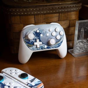 May include: White gaming controller with a blue and white wave design. The controller has a cross-shaped directional pad and several buttons. A matching set of controller accessories are also visible.