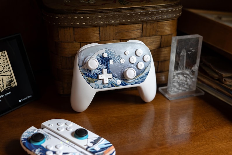 May include: White gaming controller with a blue and white wave design. The controller has a cross-shaped directional pad and several buttons. A matching set of controller accessories are also visible.