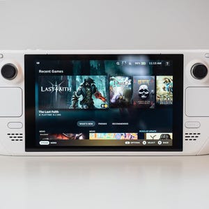 May include: A white handheld gaming console with a black screen displaying a list of recent games, including "Last Faith", "Dust", and "Morphite". The console has two analog sticks and a directional pad.