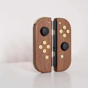 May include: A pair of wooden Nintendo Switch Joy-Con controllers with gold buttons. The controllers are connected to each other and have a black center section.