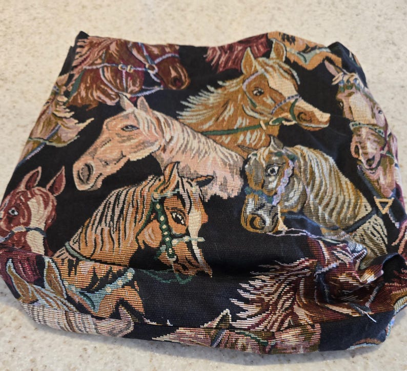 May include: A black fabric textile featuring a repeating woven pattern of horse heads in various shades of brown, tan, and cream. The horses are depicted with detailed manes and bridles, creating a dense, multi-colored equestrian design.