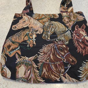 May include: A black tote bag featuring a woven tapestry pattern of multiple horse heads in shades of brown, tan, and white. The bag has two matching fabric handles and a rectangular shape, showcasing detailed equine portraits across the entire surface.