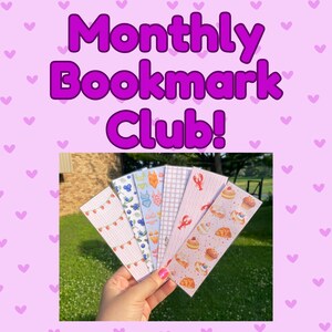 May include: A hand holds a fan of colorful bookmarks with various patterns, including strawberries, blueberries, swimwear, and pastries. The text "Monthly Bookmark Club!" is displayed in purple on a pink background.