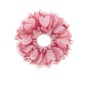 Op de afbeelding: Een roze haarband met een witte kantversiering en een hartjespatroon.