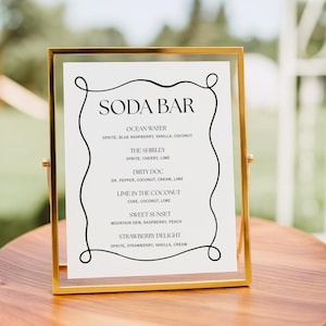 Könnte beinhalten: Ein goldgerahmtes Schild mit der Aufschrift "SODA BAR" oben. Das Schild listet verschiedene Soda-Getränke-Rezepte auf, darunter "Ocean Water", "The Shirley" und "Dirty Doc". Das Schild steht auf einem Holztisch.