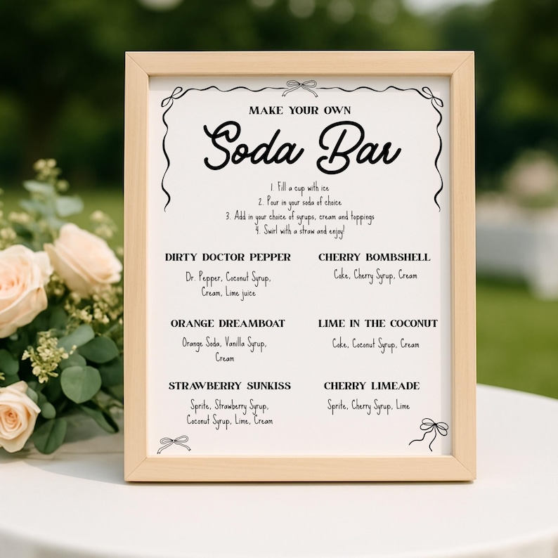 May include: A framed sign with the words "MAKE YOUR OWN Soda Bar" in elegant script. The sign lists soda bar recipes like "Dirty Doctor Pepper" and "Cherry Bombshell" with ingredients. The frame is light wood, and the background is blurred.