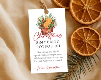 May include: A white tag with the text "Christmas Simmering Potpourri" and instructions. The tag features a watercolor illustration of a pot with oranges, cinnamon sticks, and greenery. Dried orange slices are scattered around the tag.