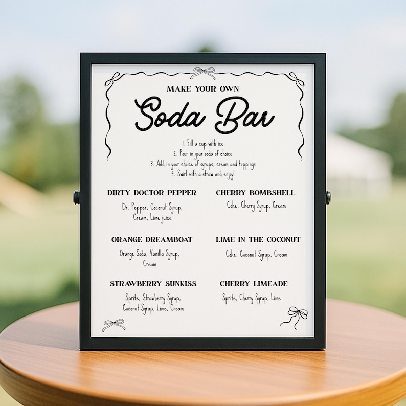 May include: A framed sign with the text "MAKE YOUR OWN Soda Bar" in elegant script. The sign lists instructions and soda recipes like "Dirty Doctor Pepper" and "Cherry Bombshell" with ingredients. The sign is black with a white background.