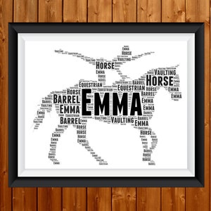 Op de afbeelding: Zwart omkaderde print met een paardensilhouet gemaakt van woorden. De naam "EMMA" staat centraal, met woorden als "HORSE", "VAULTING", "BARREL" en "EQUESTRIAN" die het paard vormen. Op een houten achtergrond.
