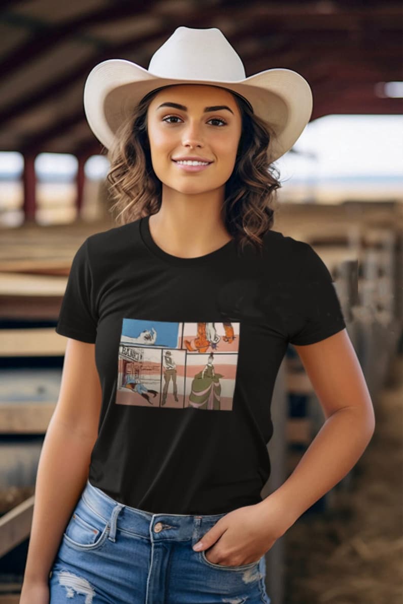 May include: A woman wearing a black t-shirt with a comic book style graphic of a cowboy and a saloon. The graphic has the text "SALOON" on the building. She is wearing a white cowboy hat and blue jeans.