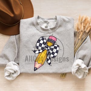 May include: A grey sweatshirt featuring a yellow pencil with a black and white chequered bow. The text "All Out Designs" is printed on the sweatshirt.