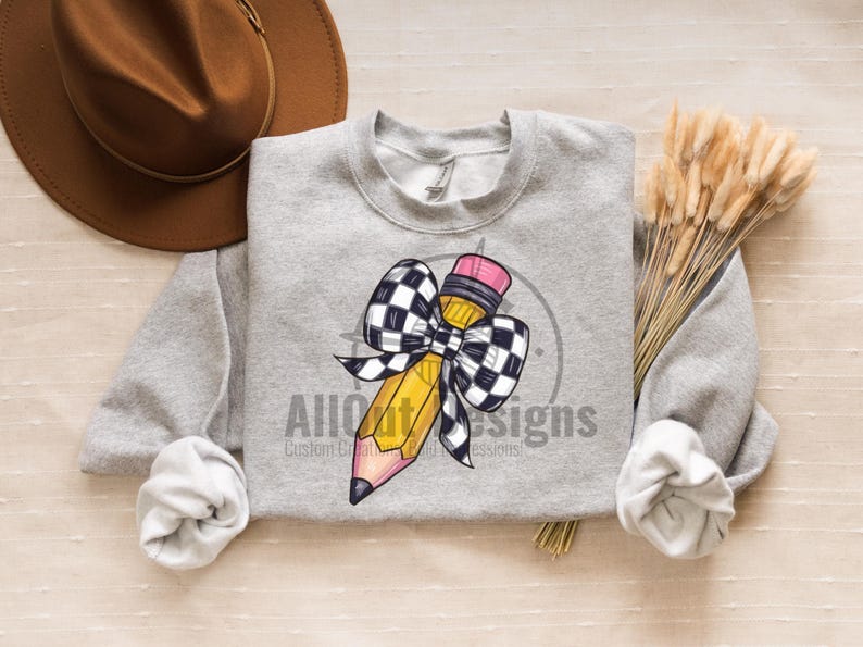 May include: A grey sweatshirt featuring a yellow pencil with a black and white chequered bow. The text "All Out Designs" is printed on the sweatshirt.