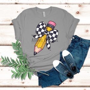 May include: A grey t-shirt featuring a yellow pencil with a black and white chequered bow.