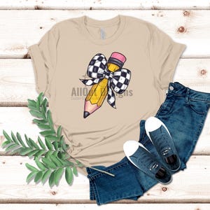 May include: A tan t-shirt featuring a yellow pencil tied with a black and white chequered bow. The pencil has a pink eraser.