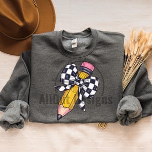 May include: A grey sweatshirt featuring a yellow pencil tied with a black and white chequered bow. The pencil has a pink eraser.